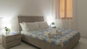 A neatly made bed with a floral bedspread, a wooden headboard, and white pillows. There is a nightstand with a lamp and a small plant. - La Terrazza sul Porto (Dorgali)