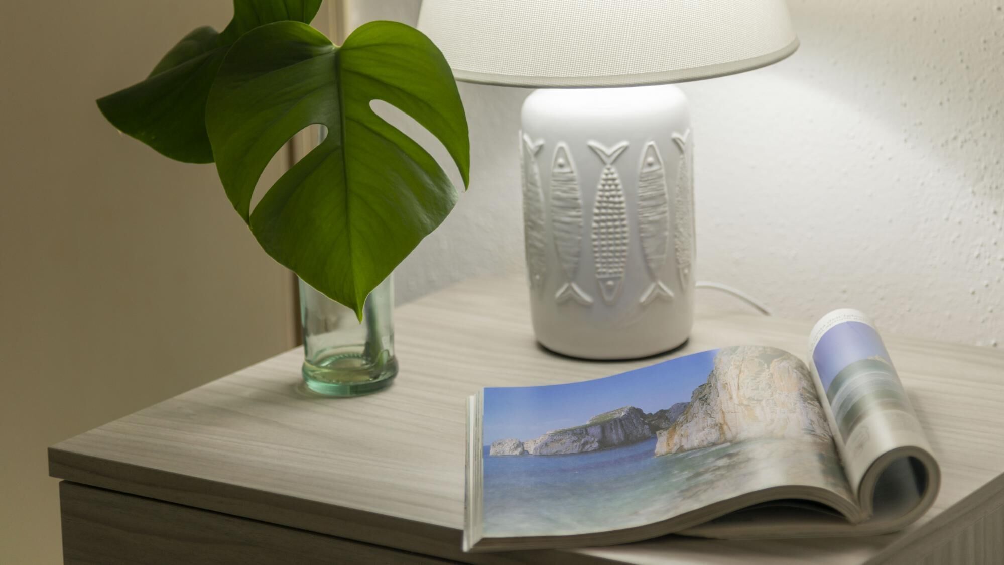 Une table de chevet en bois, avec une lampe, une plante et un magazine ouvert.