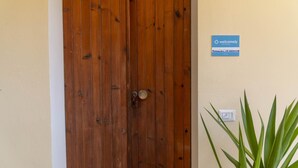 A wooden door with a keyhole and a metal keyring, a welcome sign, and a wall socket with a plant beside it. - La Terrazza sul Porto (Dorgali)