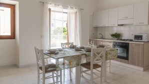 A kitchen with white cabinets, a gas stove, a microwave, and a dining table with chairs. - La Terrazza sul Porto (Dorgali)