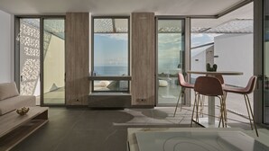 A modern interior with a sofa, a dining table with chairs, and large windows offering a view of the sea. - Porphyra Collection Villas Porto Heli  (Ermionida)