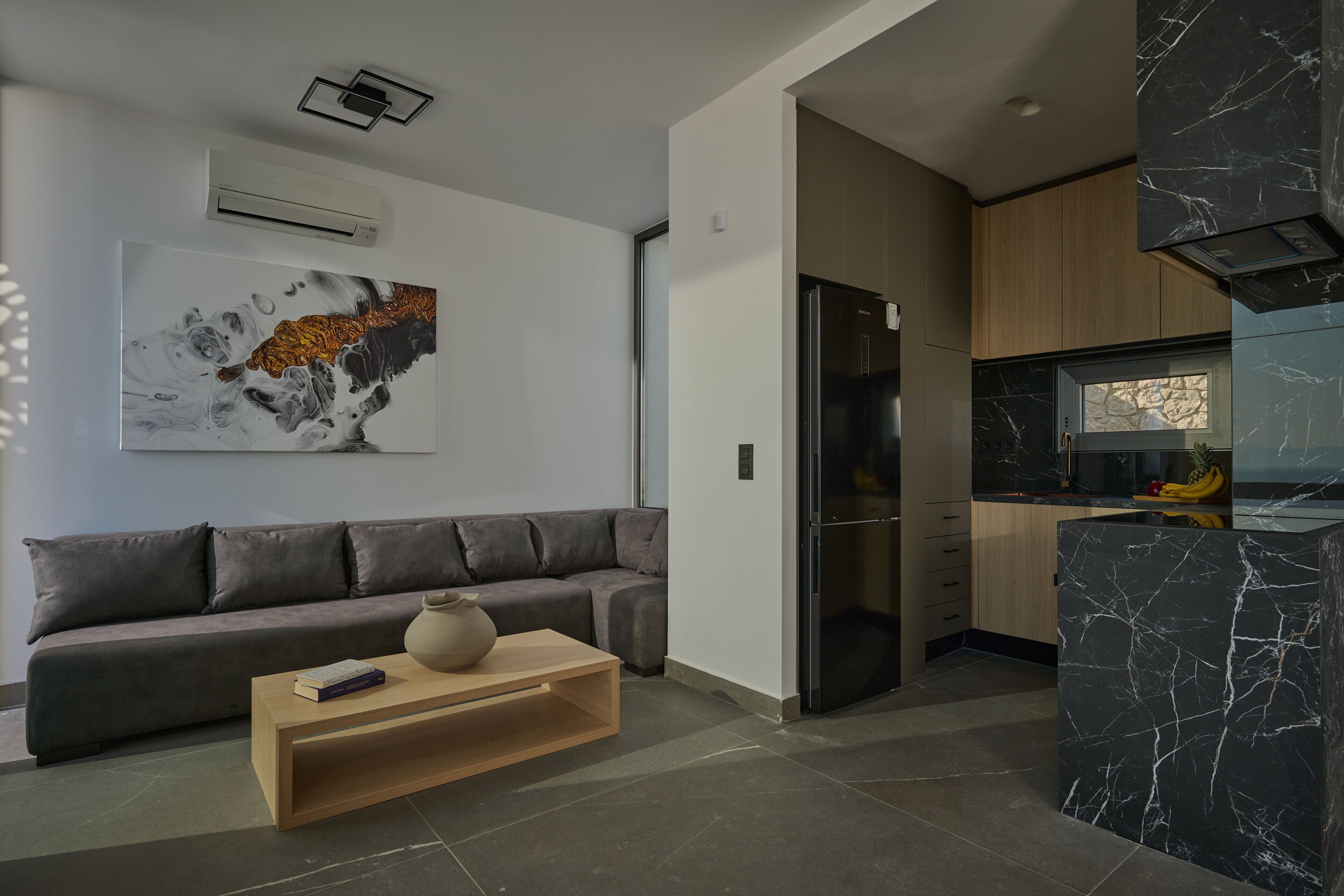 Una sala de estar moderna con un sofá gris, una mesa de centro de madera y una isla de cocina de mármol negro.