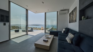 A modern living room with a large glass door leading to a balcony with a scenic view. - Porphyra Collection Villas Porto Heli  (Ermionida)