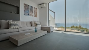 A modern living room with a large window offering a view of the sea. - Porphyra Collection Villas Porto Heli  (Ermionida)