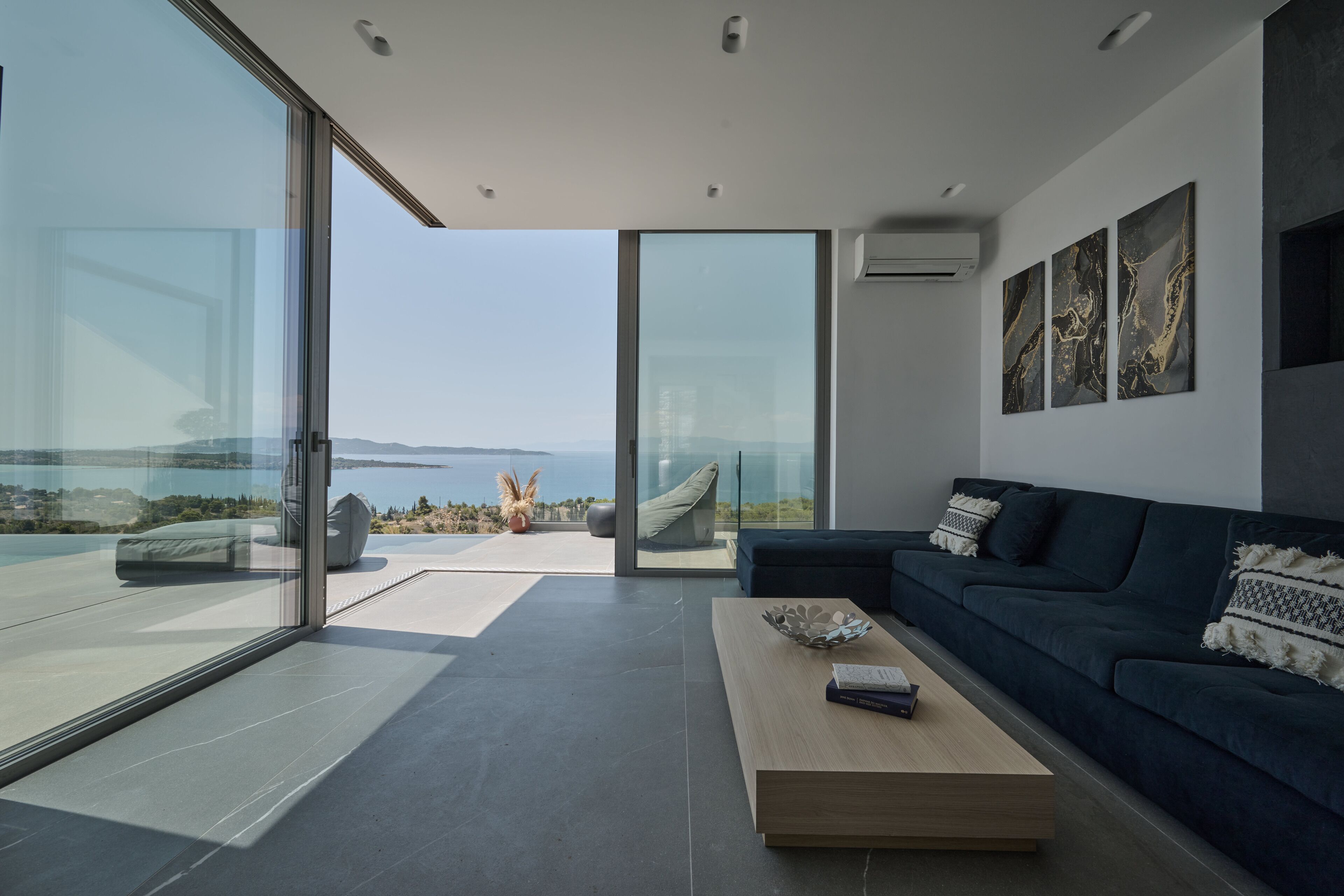 Ein modernes Wohnzimmer mit einem dunkelblauen Sofa, einem Holztisch und einer großen Glasdoor, die auf einen Balkon mit Meerblick führt.