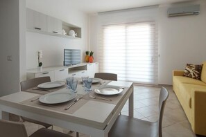 A modern kitchen with white cabinetry, a dining table set for four, and a yellow sofa in the living area. - Welcomely- Xenia Boutique House - Apt 11 (Olbia)