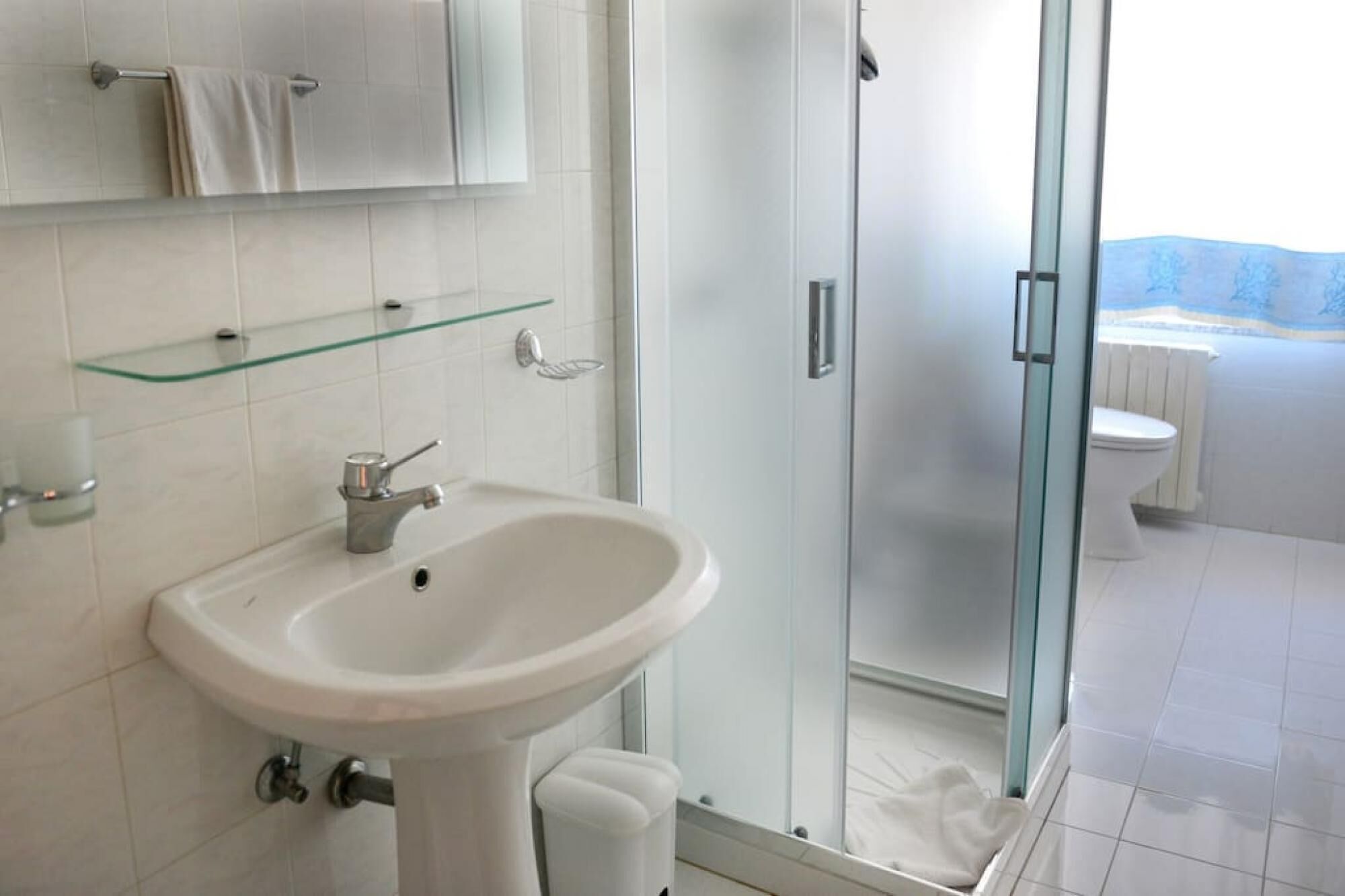 A bathroom with a glass shower enclosure, a white sink, and a toilet.