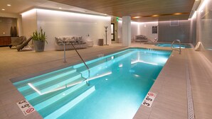 En indendørs swimmingpool med klart vand, dybdemarkeringer og et træloft.