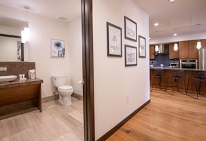 Enjoy a spacious bathroom with a large mirror, sink, and toilet, plus a kitchen area with stainless steel appliances and bar stools.