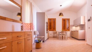 A modern kitchen with wooden cabinets, a dining area with two chairs, and a large window with wooden shutters. - Welcomely - Badde Nuraghe (Magomadas)