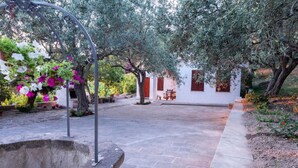 A courtyard with a white building, a stone fountain, and flowering plants. - Welcomely - Badde Nuraghe (Magomadas)