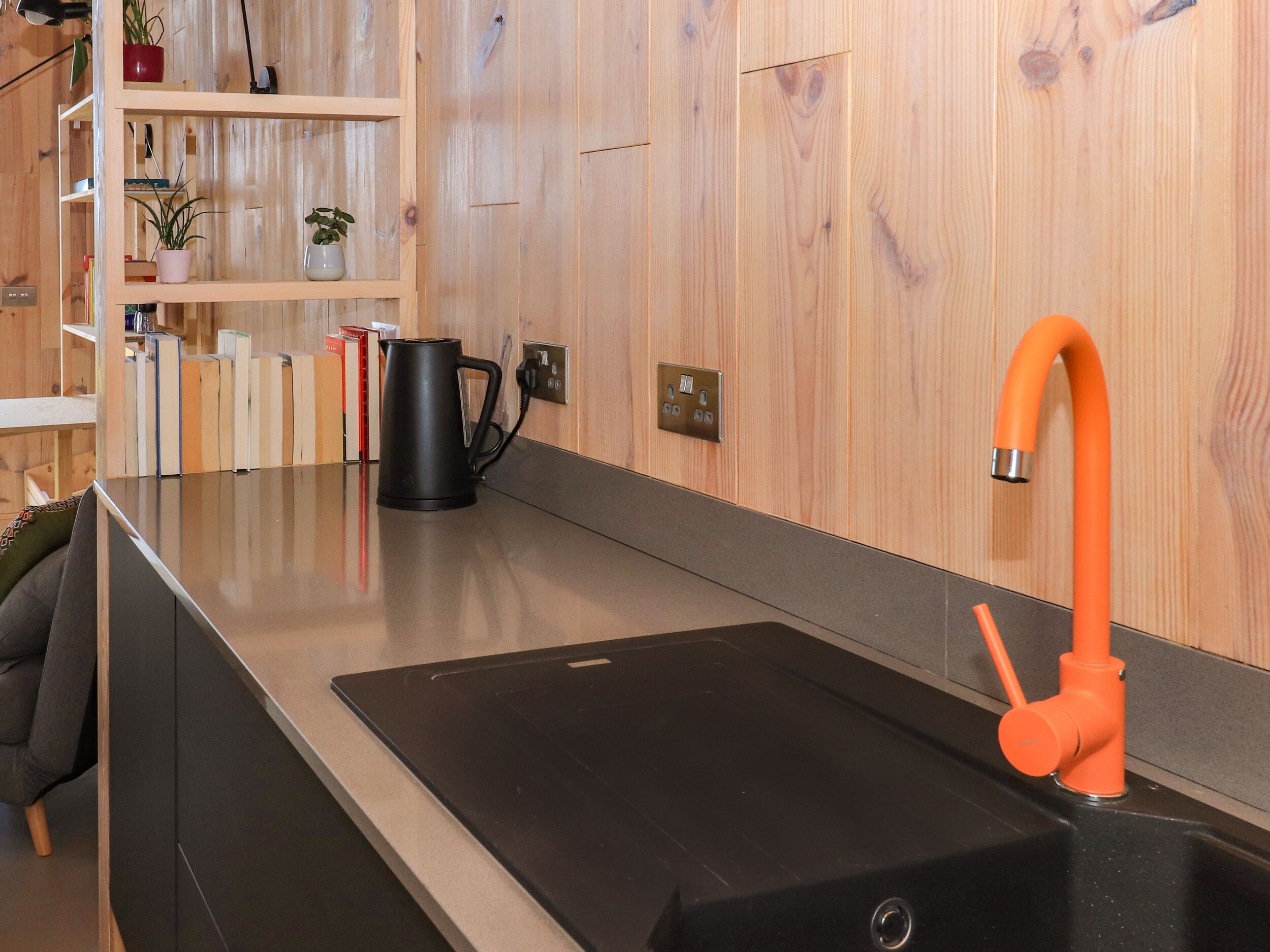 A modern kitchen with a black sink, wooden panel walls, and a bright orange faucet.
