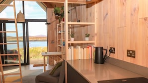 A modern kitchen with wooden cabinets, a black kettle, and a view of a lake. - North Light Studio (Isle of North Uist)