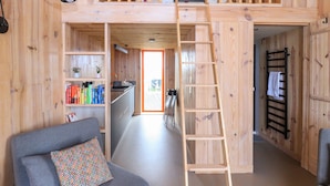 A loft-style room with a wooden interior, a grey sofa, a ladder, a small kitchenette, and a view through an open door. - North Light Studio (Isle of North Uist)