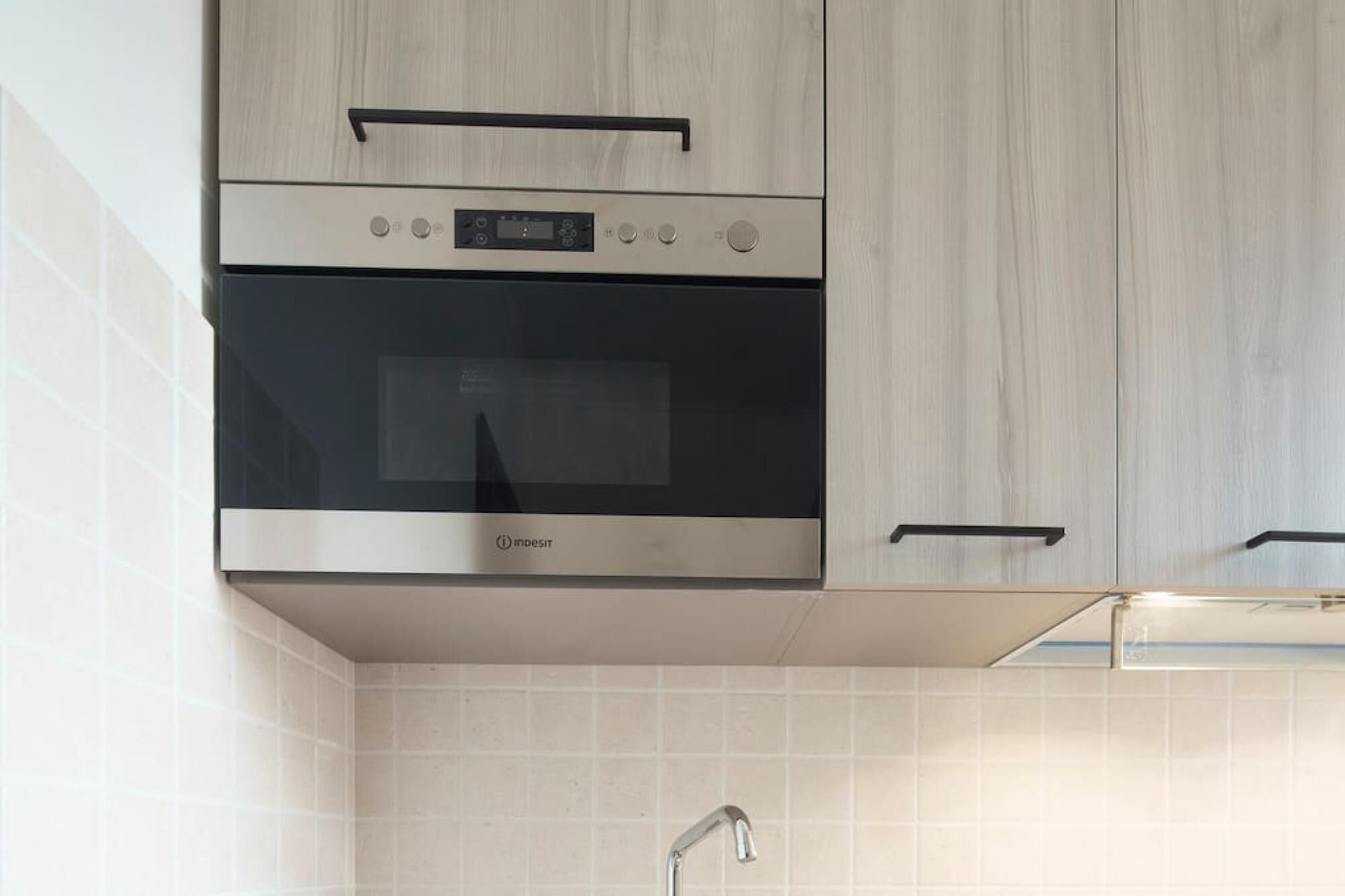 A kitchen with a built-in oven and microwave, wooden cabinets, and a tiled backsplash.