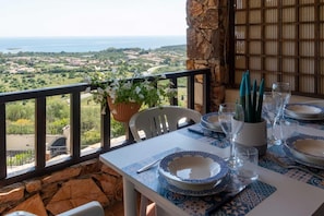 A balcony table set with plates, glasses, and a plant, overlooking a scenic landscape. - Welcomely - Casa Della Luna (Budoni)