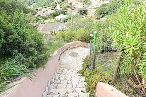 A stone staircase leading down a hillside, surrounded by lush greenery and a residential area in the background.