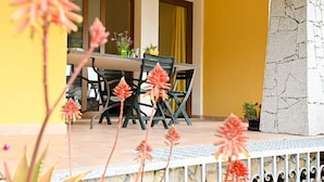 An outdoor dining area with a table and chairs, a yellow wall, and a stone wall. - Welcomely - Villa Alba (Muravera)