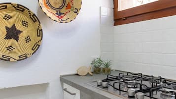 Una cocina con estufa a gas, dos cestas tejidas en la pared y una pequeña planta en maceta sobre la encimera.
