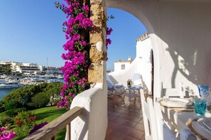 A balcony with white chairs, a table set for dining, and a view of the marina.