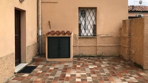 Un pequeño patio con suelo de baldosas, una puerta, una ventana con rejas y una pared con antena parabólica.