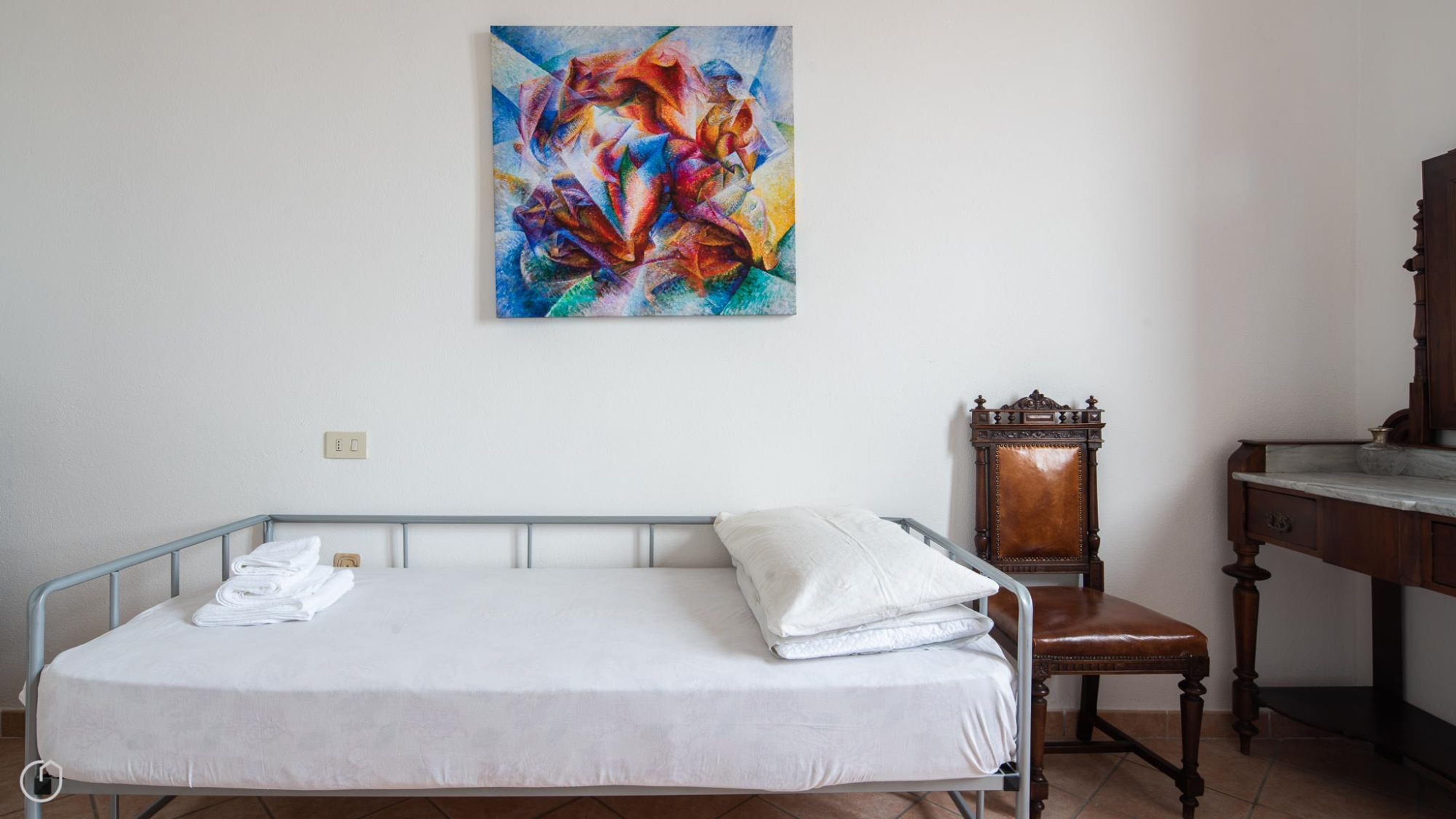 A neatly made bed with white linens, a wooden chair, and a desk with a mirror.