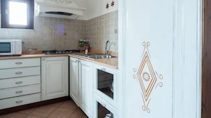 Cocina con armarios blancos, microondas, estufa y pileta. Se observa un diseño decorativo en la pared derecha.