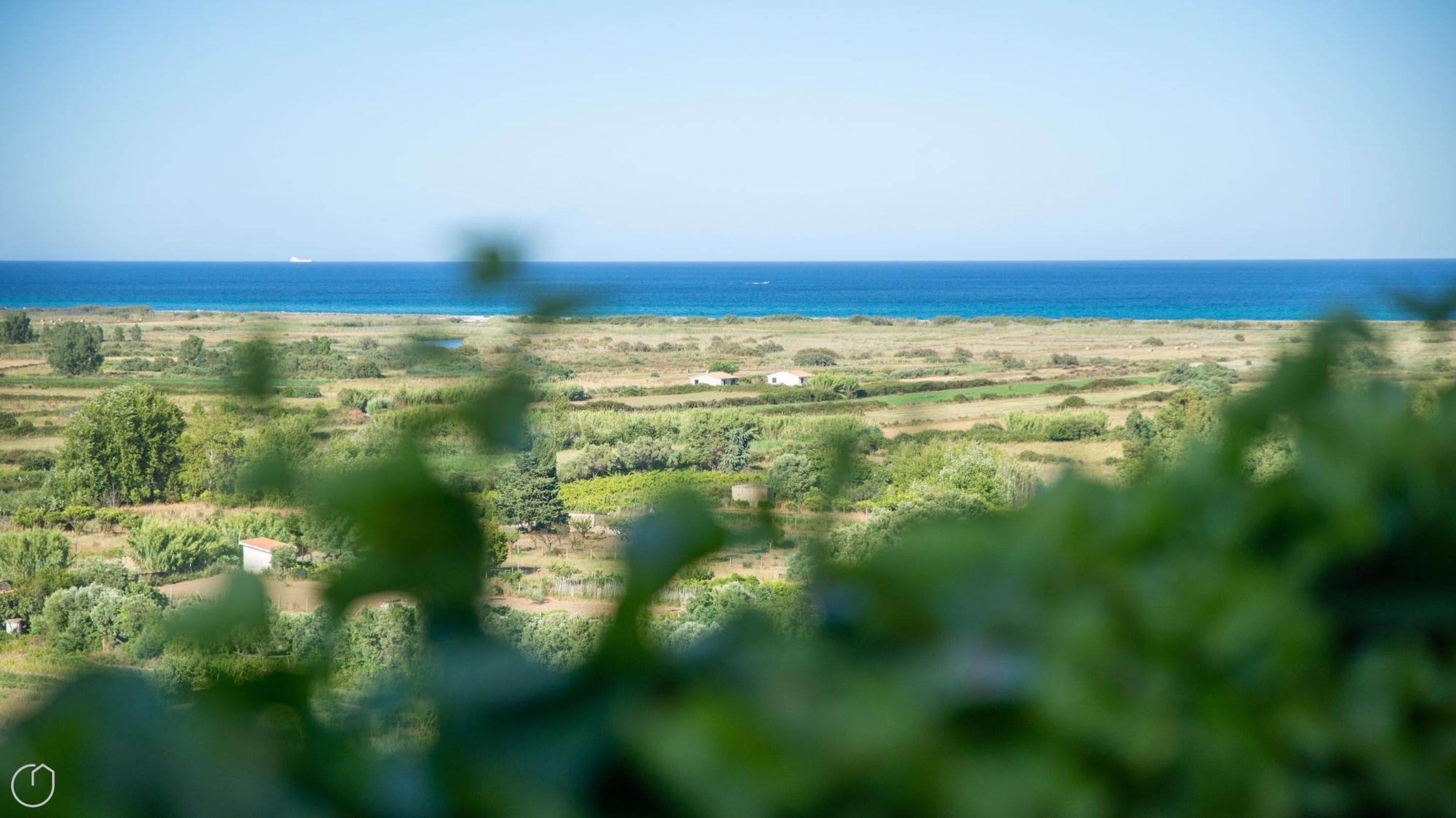 A coastal landscape with a view of the sea, green fields, and scattered buildings.