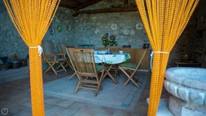 A rustic dining area with a stone wall, wooden chairs, a round table with a white tablecloth, and a flower vase. - Welcomely - Casa Tipica Vista Mozzafiato (Posada)