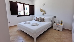Quarto bem arrumado com cama, almofadas, mesa de cabeceira e um objeto decorativo na parede.