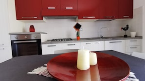 Cozinha moderna com armários vermelhos, fogão a gás e uma mesa de jantar com uma tigela vermelha e velas.