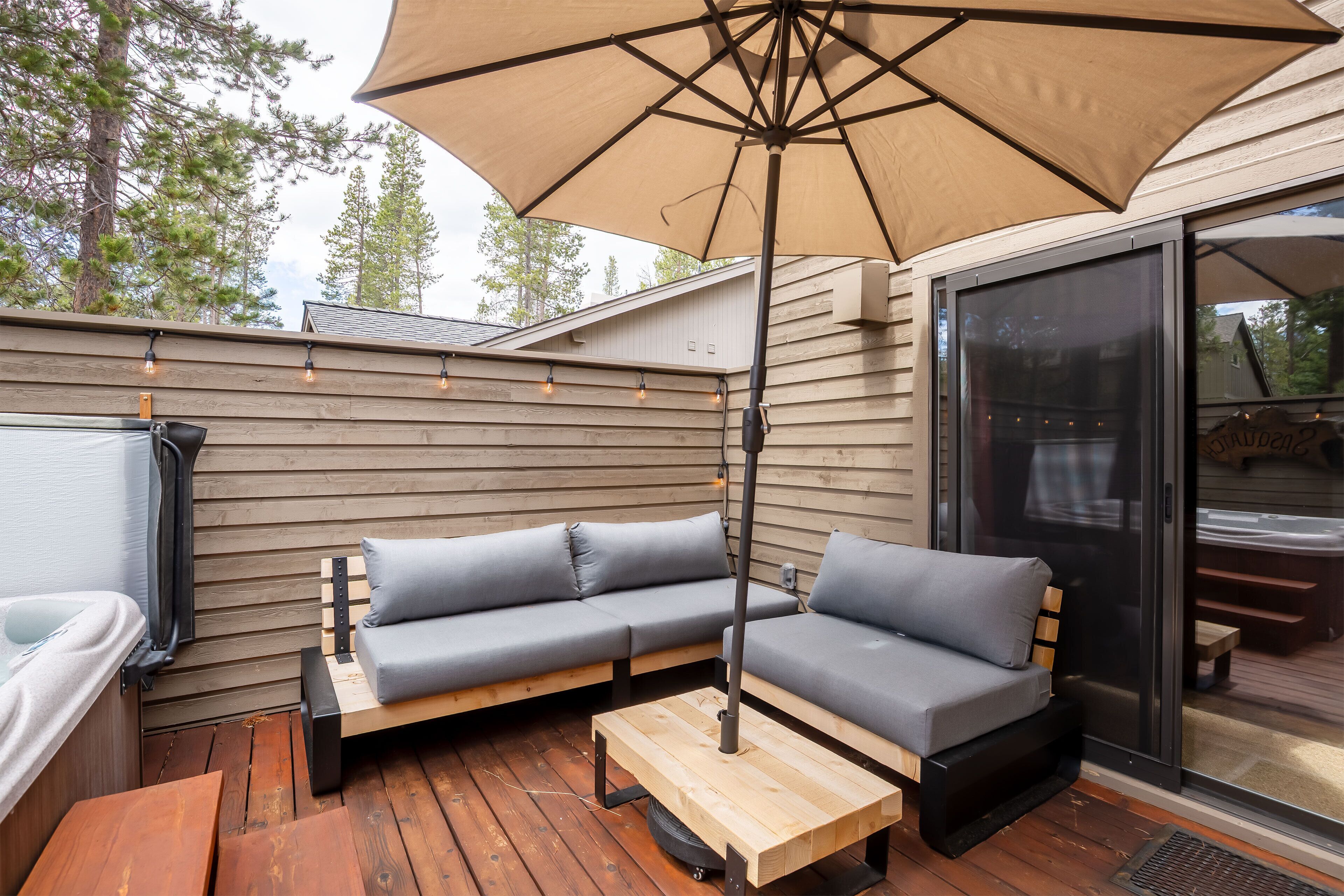 Un espace extérieur aménagé avec une terrasse en bois, un grand parasol et un canapé avec des coussins.