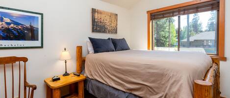 A bedroom with a bed, a nightstand, a chair, a lamp, and a window with a view of trees.