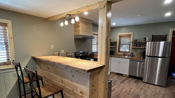 A modern kitchen with a wooden island, bar stools, stainless steel appliances, and a herringbone-patterned floor.