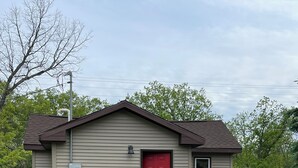 A small, single-story building with a red door, a small window, and a chimney.