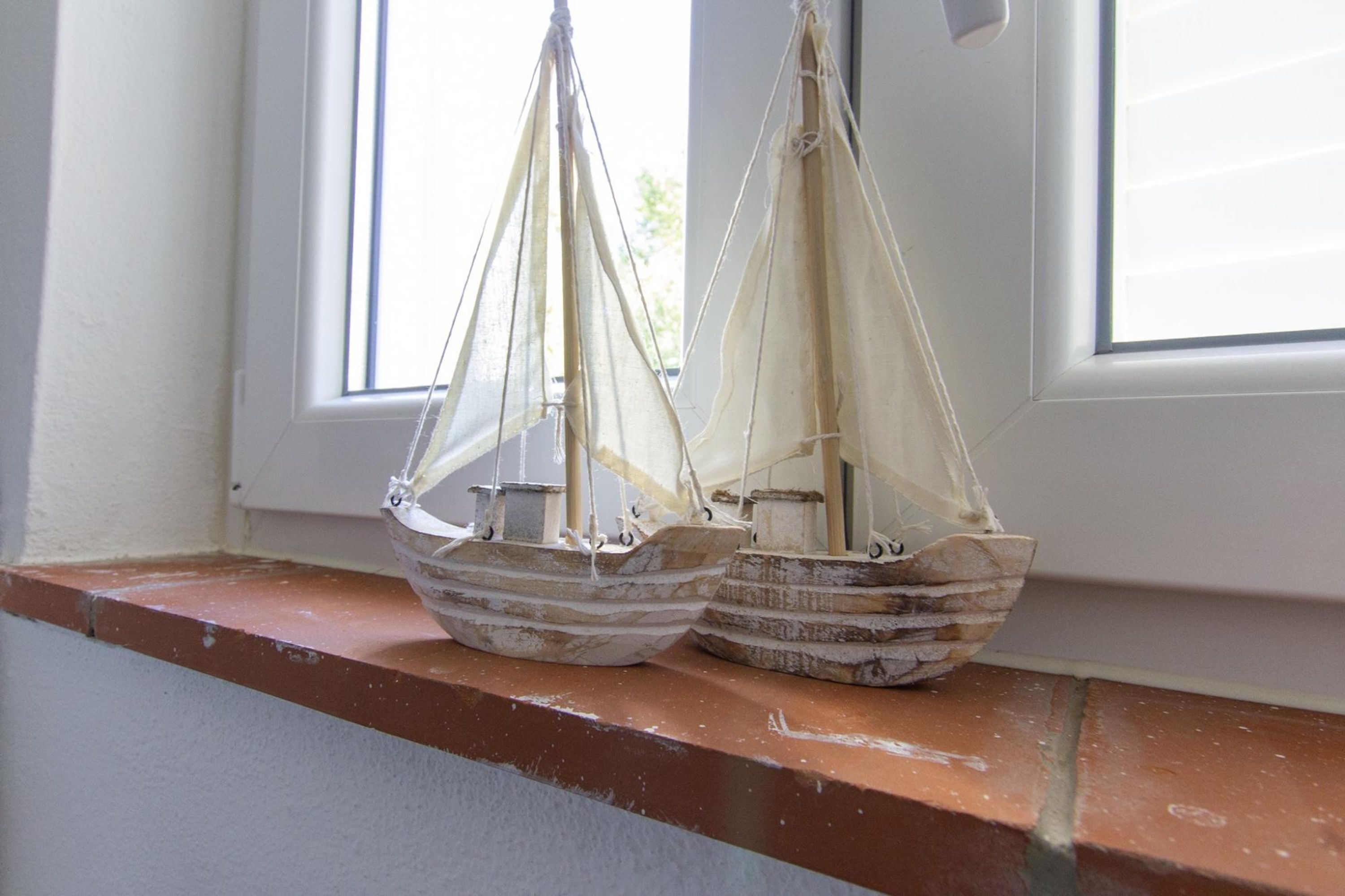 Two model sailboats on a window sill.
