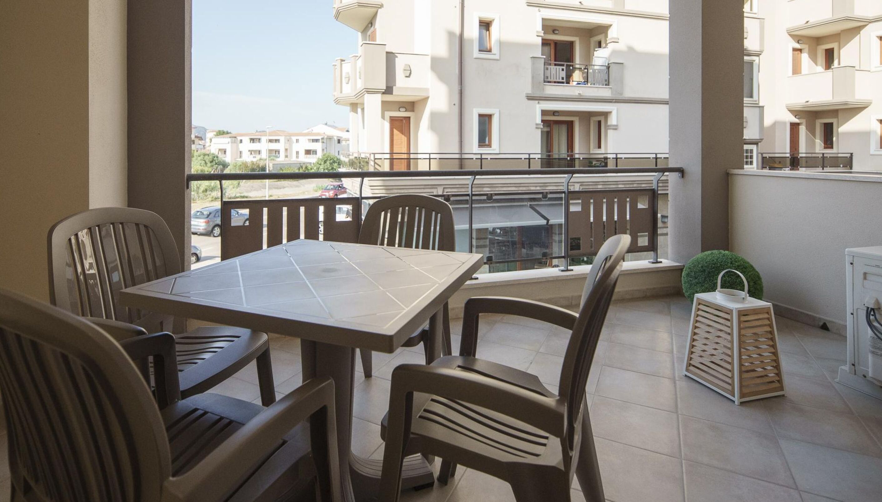 En balkon med et bord, stole, en lille plante og et hvidt skab.