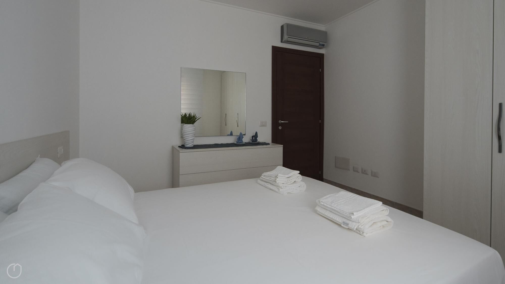 A hotel room with a bed, a bedside table with a mirror, a dresser, and a door.