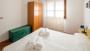 Una habitación de hotel con una cama, un armario de madera, un aparador verde y una ventana con cortinas.