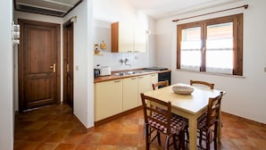 Una cocina compacta con comedor, que presenta una puerta de madera, suelo de baldosas y un ventanal con cortinas.