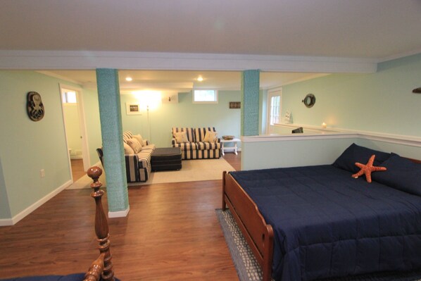 A bedroom with a bed, a starfish decoration, a wooden floor, and a view of another room.