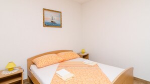 A neatly made bed with a patterned bedspread, a bedside lamp, and a small table with a lamp on it. - Apartments Skurla - Studio Apartman (Mljet)
