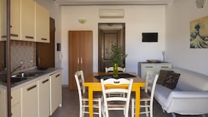A compact kitchen with a dining area, a sofa, and a TV. - Welcomely - Sa Murta-il Mirto (Tortoli)