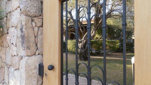A stone wall and a wrought iron gate with a tree in the background. - Welcomely - Sa Murta-il Mirto (Tortoli)