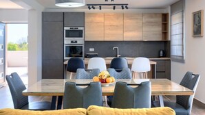 Een moderne keuken met inbouwapparatuur, een eethoek met een glazen tafel en een bank met gele kussens.