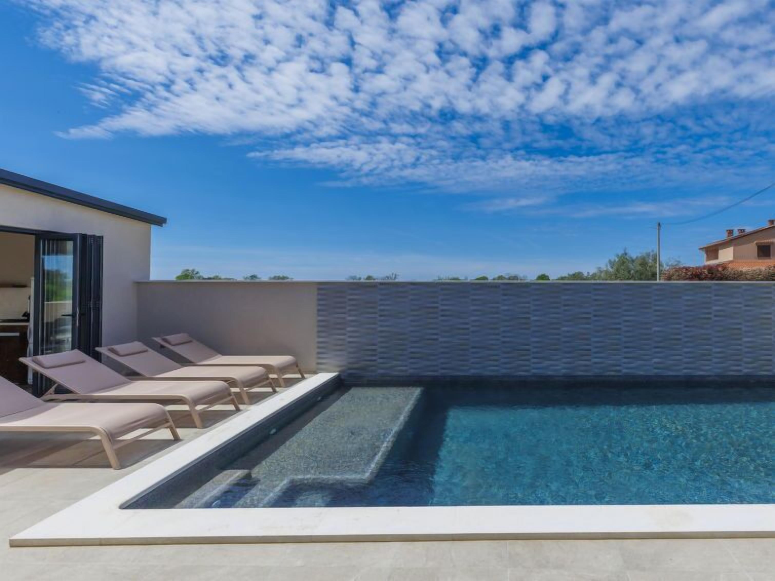 A modern outdoor pool area with lounge chairs and a clear blue sky.