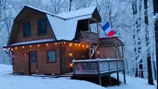 Una cabaña de madera con balcón y terraza, rodeada de árboles cubiertos de nieve.