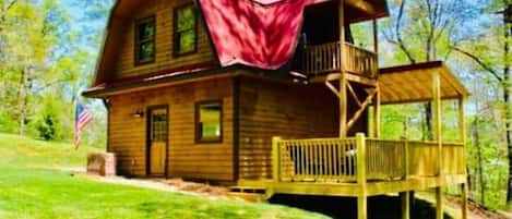 A wooden cabin with a porch and a balcony, surrounded by trees.