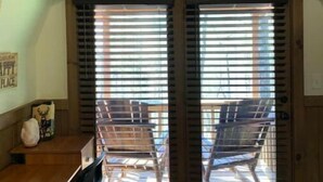 Una habitación con un escritorio de madera, dos sillas y un ventanal con persianas.