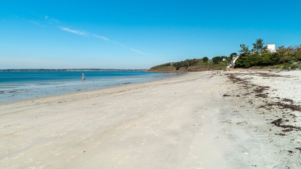 A beach with clear blue water, sandy shore, and a few buildings in the background. - Les Thermes 532 - Vue mer avec piscine partagée (Concarneau)